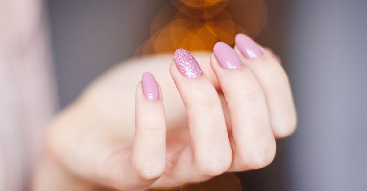 A close-up of a woman's hand displaying a stylish pink glitter manicure, highlighting nail art details.